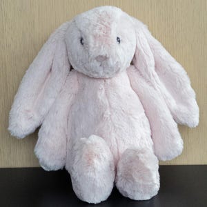May include: A soft, light pink bunny toy with long, floppy ears and a fluffy texture. The bunny has small, dark eyes and a rounded nose. The toy is designed for comfort and is suitable for children.
