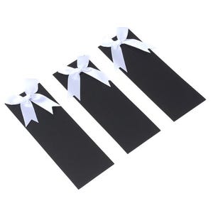 Puede incluir: Tres cajas de regalo rectangulares negras con lazos de satén blanco. Las cajas están dispuestas en diagonal sobre un fondo blanco. Los lazos están atados en la parte superior de cada caja.