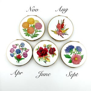 May include: Five vintage compact mirrors with floral designs. Each compact features a different flower arrangement and the month name: Nov, Aug, Apr, June, and Sept. The compacts have a gold-colored trim and a white background.