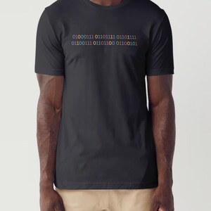 Puede incluir: Una camiseta negra con un diseño de código binario de colores impreso en la parte delantera. El código dice "01000111 01101111 01101111 01100111 01100111 01101100 01100101".