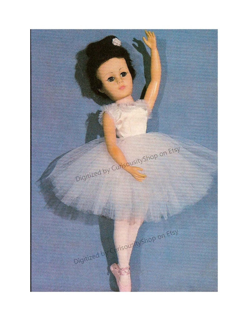 May include: A vintage ballerina doll with a white tutu, a white bodice, and pink ballet shoes. The doll has dark hair and brown eyes. The doll is posed with one arm raised and the other arm at her side. The doll is standing on a blue background.