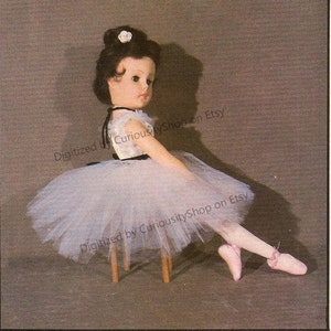 May include: A porcelain doll dressed in a white tulle tutu and a black and white bodice. The doll is sitting on a wooden stool with one leg extended and her foot pointed. The doll has brown hair and a white flower in her hair.
