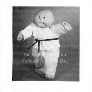 Könnte beinhalten: Eine Cabbage Patch Kid Puppe, die einen weißen Karate-Anzug mit einem schwarzen Gürtel trägt. Die Puppe steht mit einem erhobenen Bein und einem ausgestreckten Arm.