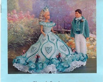 May include: A crochet pattern for a doll's dress and suit. The dress is a white and blue ball gown with a lace trim. The suit is a blue jacket with white pants. The pattern is titled "Belle of the Ball Fashion Doll Costumes" and is by Mary Layfield's Creations.