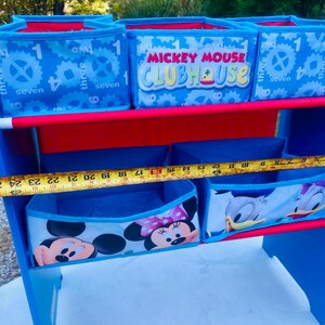 Puede incluir: Unidad de almacenamiento azul y roja para ni&ntilde;os con m&uacute;ltiples compartimentos. La unidad presenta dise&ntilde;os de Mickey Mouse Clubhouse y otros personajes de Disney. La unidad mide aproximadamente 69 cm de ancho.