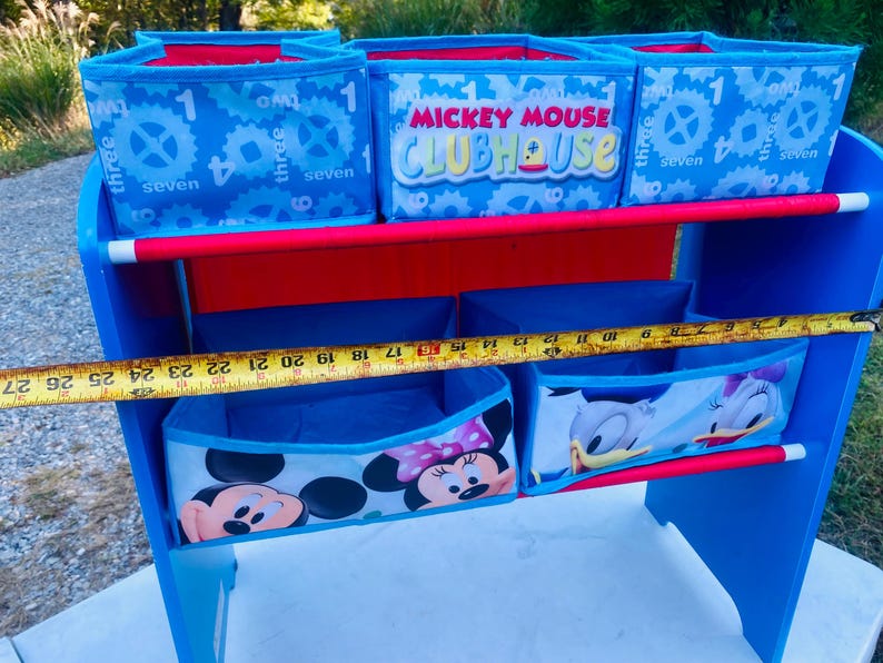 Puede incluir: Unidad de almacenamiento azul y roja para ni&ntilde;os con m&uacute;ltiples compartimentos. La unidad presenta dise&ntilde;os de Mickey Mouse Clubhouse y otros personajes de Disney. La unidad mide aproximadamente 69 cm de ancho.