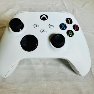 May include: A white wireless video game controller featuring two black analog sticks, a black circular directional pad, and four action buttons labeled Y, B, A, and X in yellow, red, green, and blue. The center includes an Xbox logo button.