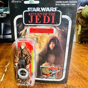 Könnte beinhalten: Eine Vintage Star Wars: Rückkehr der Jedi-Ritter Actionfigur von Luke Skywalker, noch in der Originalverpackung. Die Verpackung zeigt den Filmtitel, den Namen der Figur und eine Warnung vor Kleinteilen. Die Figur ist eine "Deleted Scene Blu-Ray Figure."