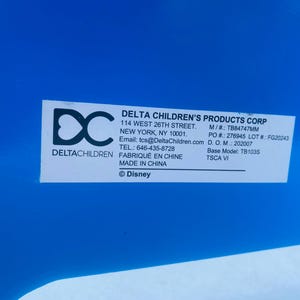 Puede incluir: Una etiqueta blanca con texto negro sobre un fondo azul. La etiqueta incluye el texto "DELTA CHILDREN'S PRODUCTS CORP", direcci&oacute;n, informaci&oacute;n de contacto y "&copy; Disney". La etiqueta tambi&eacute;n incluye el logotipo de Delta Children.