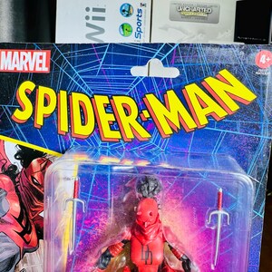 K&ouml;nnte beinhalten: Marvel Spider-Man Actionfigur in einer Kunststoffverpackung. Die Verpackung zeigt das Marvel-Logo und die Worte "Spider-Man" in Gelb und Rot. Die Figur ist eine rote Figur mit zwei silbernen Schwertern.