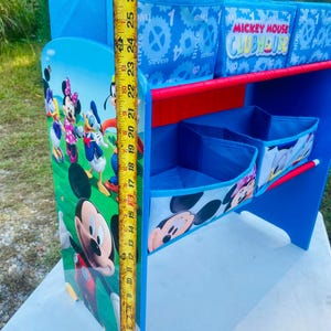 Puede incluir: Un escritorio azul y rojo de Mickey Mouse Clubhouse con compartimentos de almacenamiento. El escritorio presenta im&aacute;genes de Mickey Mouse, Minnie Mouse, Donald Duck y otros personajes. El escritorio mide aproximadamente 69 cm de alto.