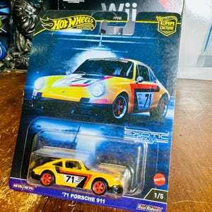 Pode incluir: Um carro de brinquedo Hot Wheels '71 Porsche 911 na embalagem. O carro é amarelo com detalhes em preto e vermelho, e o número 71 está visível. A embalagem inclui os logotipos Hot Wheels e Car Culture.