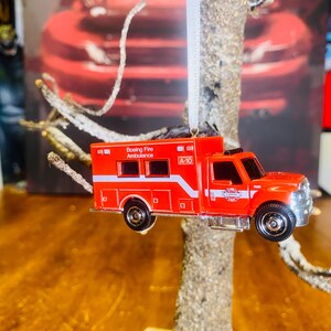 May include: Red toy fire truck ambulance ornament with the words "Boeing Fire Ambulance" and "A-10" printed on the side.