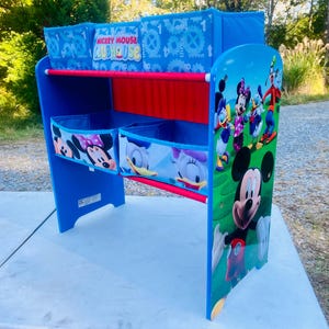 Puede incluir: Estanter&iacute;a azul para ni&ntilde;os con personajes de Mickey Mouse Clubhouse. La estanter&iacute;a tiene tres compartimentos de almacenamiento con im&aacute;genes de Mickey, Minnie y Donald Duck. El panel lateral presenta a Mickey Mouse y sus amigos.