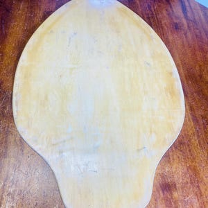 May include: A light brown wooden pizza peel with a rounded, teardrop shape.