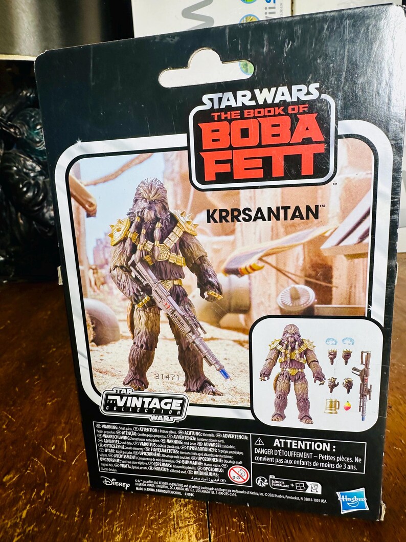 Puede incluir: Figura de acci&oacute;n de Star Wars El Libro de Boba Fett Krrsantan. La figura es marr&oacute;n y beige con detalles dorados y un rifle bl&aacute;ster. El embalaje incluye el logotipo de Vintage Collection y el logotipo de Disney.