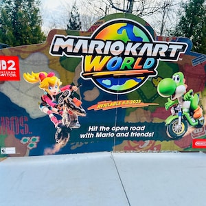 May include: A large, colourful Mario Kart World display featuring Princess Peach and Yoshi on motorcycles. The Nintendo Switch logo is visible, along with the text "Available 6.5.2025" and "Hit the open road with Mario and friends!"