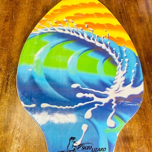May include: A blue, green, and yellow skimboard with a wave design and a white splash of water. The board has a black lizard logo with the text "Skim Lizard" and the copyright information "2003 Jon COPE All rights reserved".