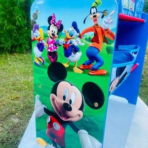 Puede incluir: Estanter&iacute;a de almacenamiento azul y blanca con Mickey Mouse y sus amigos. La estanter&iacute;a tiene m&uacute;ltiples compartimentos y est&aacute; decorada con im&aacute;genes de Mickey, Minnie, Donald Duck, Daisy Duck y Goofy. Las palabras "Mickey Mouse Clubhouse" son visibles.