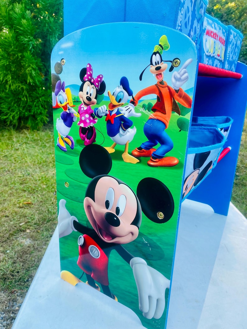 Puede incluir: Estanter&iacute;a de almacenamiento azul y blanca con Mickey Mouse y sus amigos. La estanter&iacute;a tiene m&uacute;ltiples compartimentos y est&aacute; decorada con im&aacute;genes de Mickey, Minnie, Donald Duck, Daisy Duck y Goofy. Las palabras "Mickey Mouse Clubhouse" son visibles.