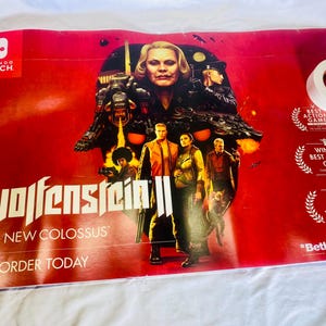 May include: A red poster for the video game "Wolfenstein II: The New Colossus" for the Nintendo Switch. The poster features a central image of characters and a skull-like structure, with the game title and "Pre-Order Today" text.