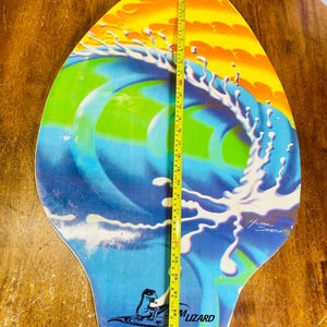 May include: A blue, green, yellow, and white surfboard with a wave design and the text "Foam Lizard" and "For COPA All Rights Reserved". The surfboard is 30 inches long.