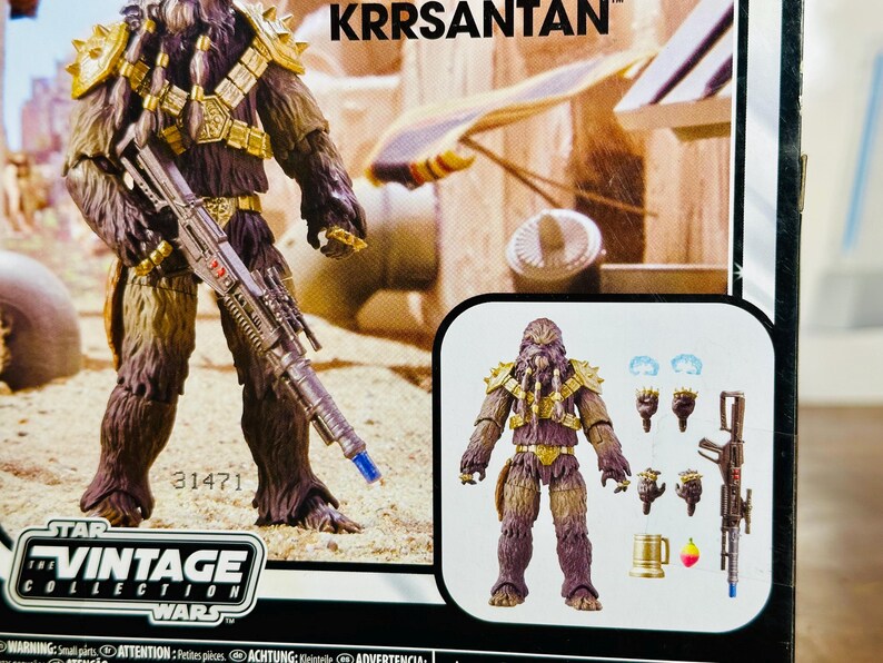 Puede incluir: Una figura de acci&oacute;n de la colecci&oacute;n Vintage de Star Wars de Krrsantan, un cazarrecompensas Wookiee. La figura es marr&oacute;n y morada con armadura dorada y un rifle bl&aacute;ster. El embalaje incluye el texto "KRRSANTAN" y "STAR WARS VINTAGE COLLECTION".