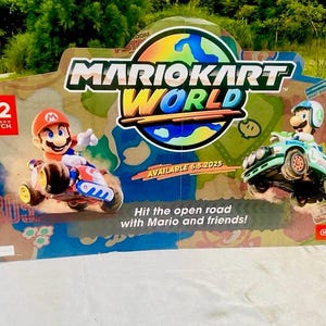 May include: A vibrant Mario Kart World display featuring Mario and Luigi in their karts. The sign includes the Nintendo Switch logo, the text "Hit the open road with Mario and friends!" and the availability date 6/5/2025.