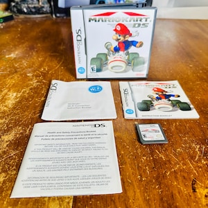Puede incluir: Un juego completo de Nintendo DS para Mario Kart DS. El juego incluye la caja del juego, el cartucho del juego, el folleto de instrucciones y otros insertos. La caja del juego presenta a Mario en un kart. El juego está clasificado E para todos.
