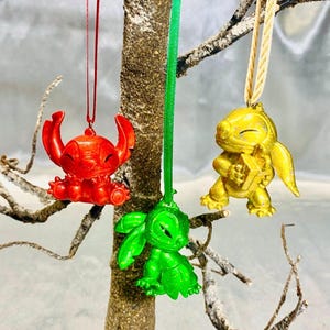 May include: Three Stitch Christmas ornaments, one red, one green, and one gold, hanging from a tree branch.