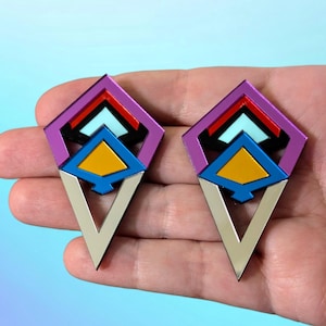May include: A pair of geometric earrings with a silver, purple, blue, yellow, and red colour scheme. The earrings are shaped like a diamond with a pointed bottom.