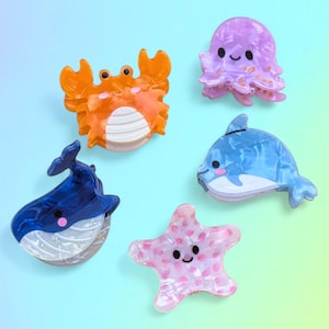 Op de afbeelding: Een verzameling van vijf haarclips met zeethema. De set bevat een krab, octopus, dolfijn, walvis en zeester, elk in levendige kleuren met een glanzende afwerking. Deze decoratieve clips zijn ideaal om een vleugje fantasie toe te voegen.