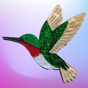 May include: A green, red and white hummingbird brooch with a glittery green body and beige wings.
