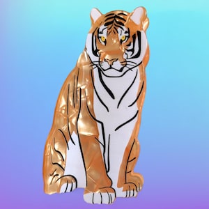 May include: A decorative tiger figurine in a seated pose. The figurine features a gold and white colour scheme with black stripes and details. The tiger's face is detailed with black stripes and yellow eyes.