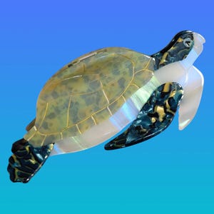 May include: A decorative sea turtle figurine with a translucent shell in shades of green and gold, accented with dark blue and gold flipper details. The turtle's head and flippers have a pearlescent sheen, set against a gradient blue background.