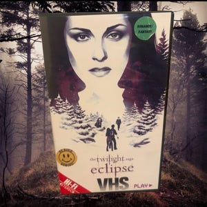 May include: A VHS tape of "The Twilight Saga: Eclipse" with a forest scene and a woman's face. The cover includes the text "ROMANCE/FANTASY", "BE KIND", "Hi-Fi STEREO", and "PLAY". The tape is in a black case.