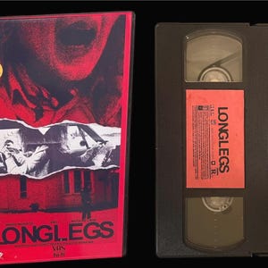 May include: A VHS tape of the horror film "Longlegs" with a red and black cover featuring a close-up of a person's mouth and a scene from the film. The tape is labeled "Longlegs" and has a "2 Day Rental" sticker.