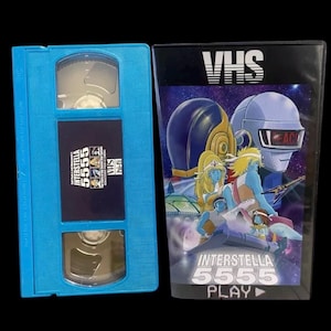 May include: A blue VHS tape and its case. The case features a colorful illustration with the text "INTERSTELLA 5555" and "PLAY". The VHS tape itself is blue with the same title and "VHS" printed on it.