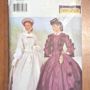May include: Butterick sewing pattern for historical costumes. The pattern features two women in Victorian-era dresses. The pattern size is 18-20-22. The cover has the text "Butterick" and "History". The dresses are in white and purple.