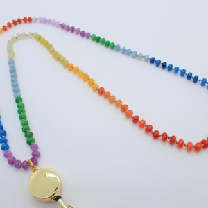 Puede incluir: Un cord&oacute;n para credencial con una larga hilera de peque&ntilde;as cuentas multicolores dispuestas en un degradado de arco&iacute;ris. Las cuentas pasan por tonos rojos, naranjas, amarillos, verdes, azules y morados. Incluye un porta-identificaci&oacute;n circular dorado.