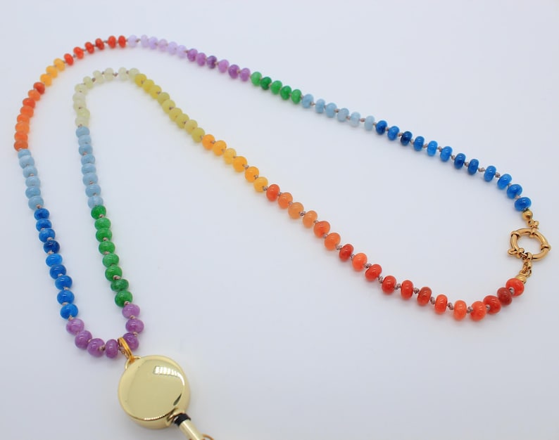 Puede incluir: Un cord&oacute;n para credencial con una larga hilera de peque&ntilde;as cuentas multicolores dispuestas en un degradado de arco&iacute;ris. Las cuentas pasan por tonos rojos, naranjas, amarillos, verdes, azules y morados. Incluye un porta-identificaci&oacute;n circular dorado.