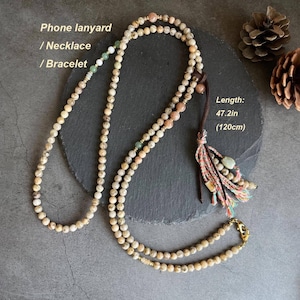 May include: Beaded necklace, phone lanyard, or bracelet. The necklace is 47.2 inches (120cm) long and features beige, peach, and green beads. It has a leather cord with a tassel and a gold-colored clasp.