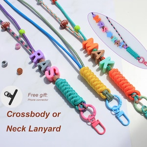 Könnte beinhalten: Drei bunte Paracord-Lanyards mit geflochtenen Abschnitten, Kunststoff-Buchstabenperlen zur Namensbildung und kleinen sportlichen Perlen. Jedes Lanyard enthält einen Metallkarabiner und einen Ring. Ein Inset zeigt den Namen MRS KAI.