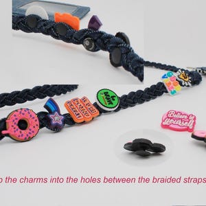 May include: A dark blue braided strap featuring various colorful charms including a pink donut, a star, and text-based charms reading "YOU'RE DOING GREAT", "be brave", and "Believe in yourself". The text "Snap the charms into the holes between the braided straps" is visible.
