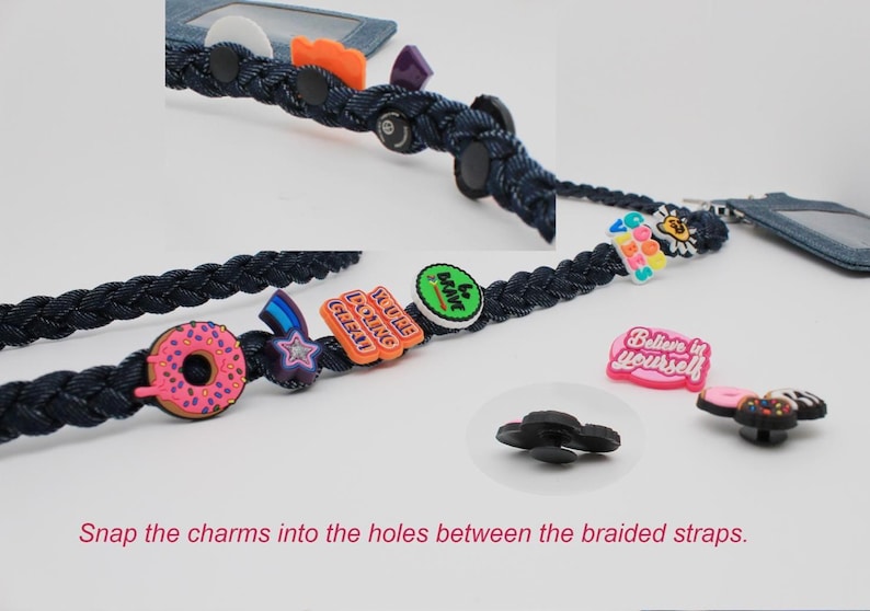 May include: A dark blue braided strap featuring various colorful charms including a pink donut, a star, and text-based charms reading "YOU'RE DOING GREAT", "be brave", and "Believe in yourself". The text "Snap the charms into the holes between the braided straps" is visible.