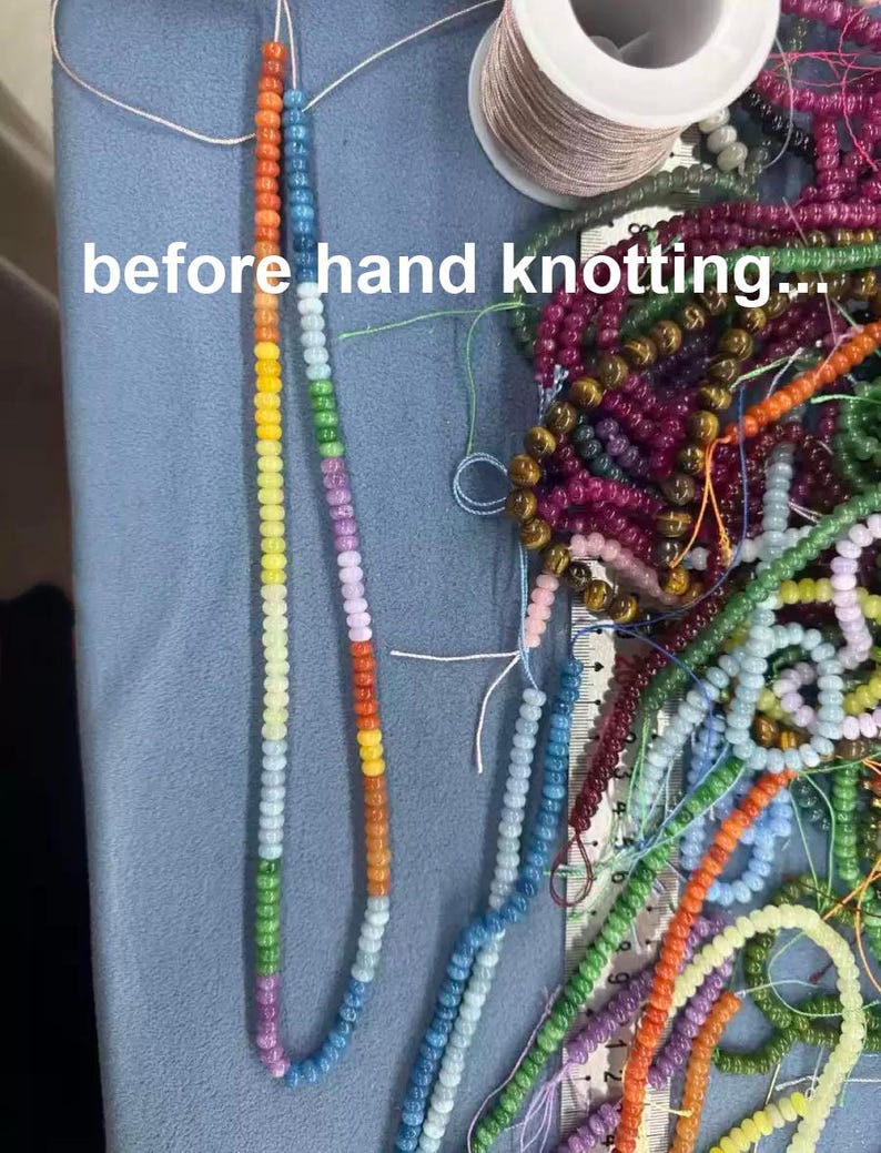 Puede incluir: Una colecci&oacute;n de cuentas de vidrio multicolor en hilos, incluyendo una hebra larga con un degradado de arco&iacute;ris y un carrete de hilo. El texto 'before hand knotting...' es visible. Una regla muestra medidas en cent&iacute;metros junto a las cuentas.