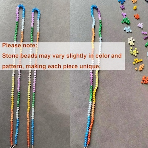 Puede incluir: Tres largos hilos de cuentas de piedra multicolor dispuestos en un patr&oacute;n vertical. Las cuentas presentan un degradado de tonos azules, morados, blancos, verdes, amarillos y naranjas. El texto superpuesto dice: Please note: Stone beads may vary slightly in color and pattern, making each piece unique.