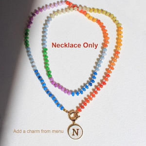 Puede incluir: Un collar de cuentas multicolor con peque&ntilde;as cuentas redondas y transl&uacute;cidas en un patr&oacute;n de degradado arco&iacute;ris. El collar incluye un cierre circular dorado con un colgante blanco que muestra la letra N. Texto: Necklace Only.