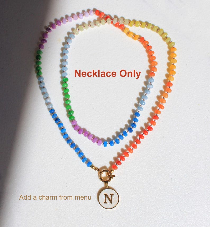 Puede incluir: Un collar de cuentas multicolor con peque&ntilde;as cuentas redondas y transl&uacute;cidas en un patr&oacute;n de degradado arco&iacute;ris. El collar incluye un cierre circular dorado con un colgante blanco que muestra la letra N. Texto: Necklace Only.