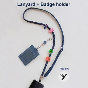 May include: A dark blue braided lanyard with a matching denim-textured badge holder. The lanyard features several small colorful charms and a retractable reel. Text at the top reads Lanyard + Badge holder and Free gift.